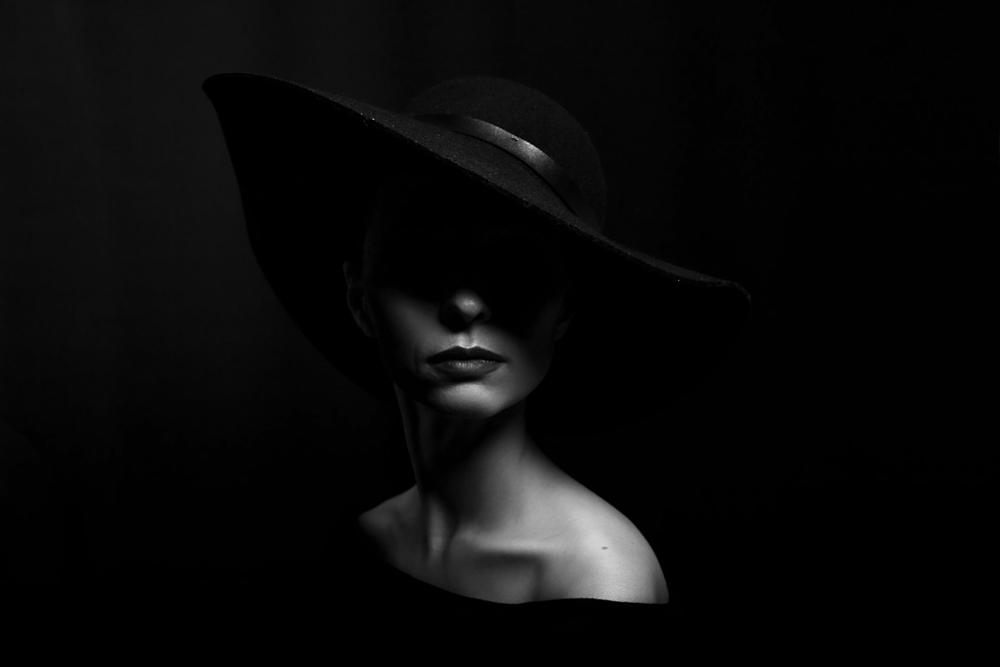 Een knappe dame met een donkere achtergrond en opgelicht gezicht. Het perfecte model voor zwart wit fotografie.