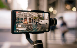 Een persoon die een prachtige zonsondergang fotografeert met een smartphone, waarbij de focus ligt op de telefoon en de levendige kleuren van de lucht op het scherm.