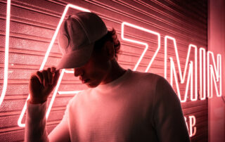 Een straatfotograaf heeft een foto genomen van een jongen die wordt verlicht door neonlicht, met een petje op zijn hoofd, wat de moderne stedelijke cultuur en mode weergeeft.