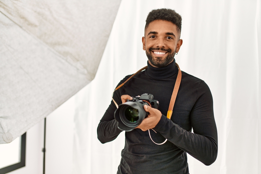Een studiofotograaf staat in de studio met een brede glimlach op zijn gezicht en houdt een camera in zijn hand vast, wat de vreugde en enthousiasme van de fotograaf voor zijn werk in de studio uitdrukt.