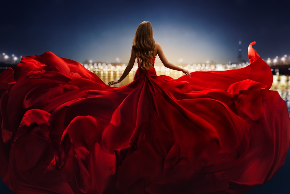 Een glamour fotograaf heeft een opname gemaakt van een vrouw in een gigantische rode jurk, gefotografeerd vanaf de achterkant, waardoor de dramatische en luxueuze uitstraling van de jurk wordt benadrukt.