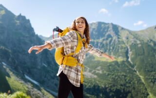 Een lifestylefotograaf heeft een foto gemaakt van een jonge vrouw met een rugzak, die boven op een berg staat, wat het avontuurlijke en actieve karakter van het buitenleven benadrukt.
