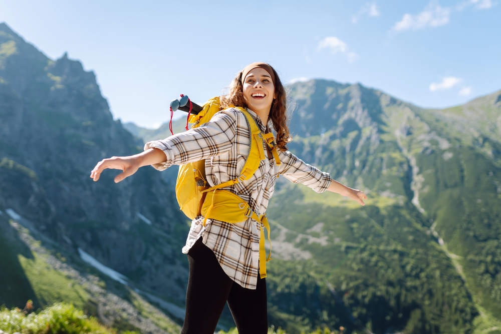 Een lifestylefotograaf heeft een foto gemaakt van een jonge vrouw met een rugzak, die boven op een berg staat, wat het avontuurlijke en actieve karakter van het buitenleven benadrukt.