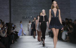 Een runwayfotograaf staat aan de zijkant van de catwalk en fotografeert modellen terwijl ze lopen, omringd door modekenners en professionals, wat de spanning en het vakmanschap van de modewereld illustreert.