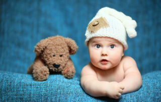 Een vrolijke baby zittend tussen kleurrijke speeltjes, kunstig vastgelegd door de babyfotograaf in een levendige setting.