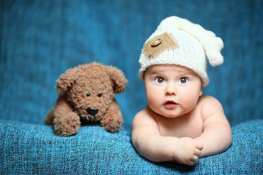 Een vrolijke baby zittend tussen kleurrijke speeltjes, kunstig vastgelegd door de babyfotograaf in een levendige setting.