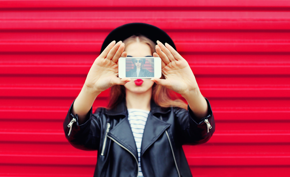 Een Instagram fotograaf heeft een selfie gemaakt van een meisje voor een rode achtergrond, waarbij de levendige kleur en de uitstraling van het meisje centraal staan.
