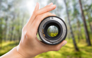 Een camera lens wordt in de hand gehouden en erdoorheen gekeken, waarbij het beeld erachter wordt vergroot, wat de kracht en het potentieel van een hoogwaardige lens in de fotografie illustreert.