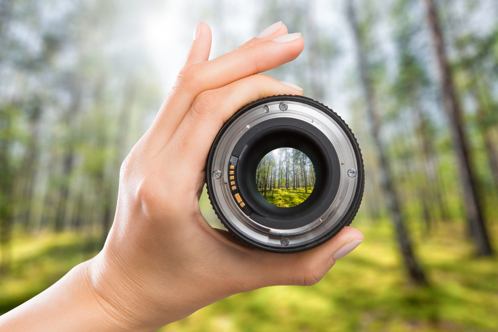 Een camera lens wordt in de hand gehouden en erdoorheen gekeken, waarbij het beeld erachter wordt vergroot, wat de kracht en het potentieel van een hoogwaardige lens in de fotografie illustreert.