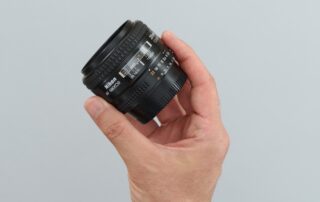 Een man die een prime lens vasthoudt in zijn hand. De prime lens, bekend om zijn vaste brandpuntsafstand, is een populaire keuze voor fotografen die streven naar hoge beeldkwaliteit en artistieke precisie. De man toont de lens met trots, klaar om deze te gebruiken om indrukwekkende foto's te maken. Deze opname benadrukt de eenvoud en de kracht van prime lenzen in de handen van een fotograaf.