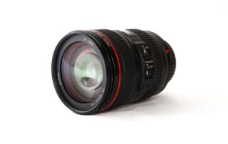 Een macro lens van Canon geplaatst op een tafel. De Canon macro lens is het hoofdonderwerp van de compositie, en het toont de merknaam Canon. Dit beeld benadrukt de macro lens, die is ontworpen om close-up opnamen met hoge precisie te maken, waardoor kleine details en texturen duidelijk zichtbaar worden.