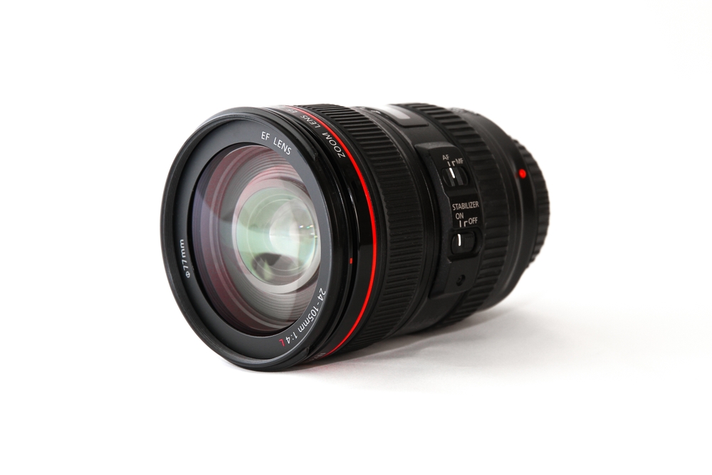 Een macro lens van Canon geplaatst op een tafel. De Canon macro lens is het hoofdonderwerp van de compositie, en het toont de merknaam Canon. Dit beeld benadrukt de macro lens, die is ontworpen om close-up opnamen met hoge precisie te maken, waardoor kleine details en texturen duidelijk zichtbaar worden.