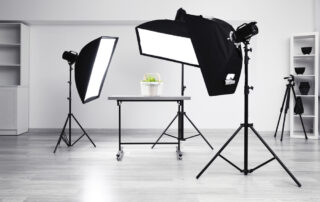 Drie grote staande studiolampen verlichten een ruime fotostudio. De lampen staan strategisch opgesteld om een gelijkmatige en professionele belichting te bieden in de studio-omgeving. De lichtbronnen werpen zachte en diffuse lichtstralen, waardoor ze ideaal zijn voor het fotograferen van onderwerpen met minimale schaduwen. De professionele uitstraling van de lampen geeft de studio een professionele en creatieve sfeer, klaar voor fotoshoots.