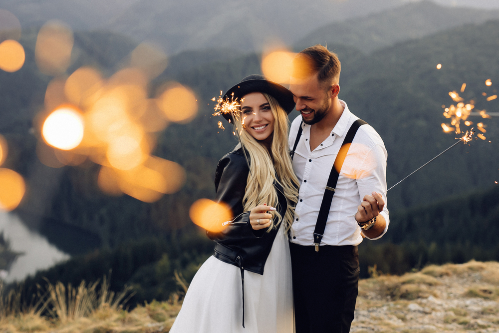 Man en vrouw poseren op een bergtop tijdens een locatie fotoshoot, met fonkelende vuurwerk sterretjes in hun handen tegen een schemerige achtergrond.
