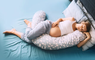 Een zwangere vrouw liggend op een bed in een slaaphouding, met een kussen tussen haar benen. Deze serene compositie legt de vrouw vast terwijl ze rust en ontspanning zoekt tijdens haar zwangerschap. Het kussen tussen haar benen kan worden gebruikt voor comfort en ondersteuning. Zwangerschapsfotografie kan momenten van rust en intimiteit vastleggen, naast het vieren van de zwangerschap zelf.