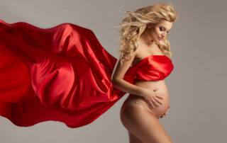 Een zwangere vrouw gehuld in een grote rode sjaal tijdens een zwangerschapsshoot. De sjaal wikkelt zich om haar lichaam en benadrukt haar zwangere buik. Deze compositie combineert de warmte van de rode sjaal met het moederschap en de verwachting van de aanstaande geboorte. Het resulteert in een beeld dat zowel elegant als symbolisch is voor de zwangerschapsfotografie.