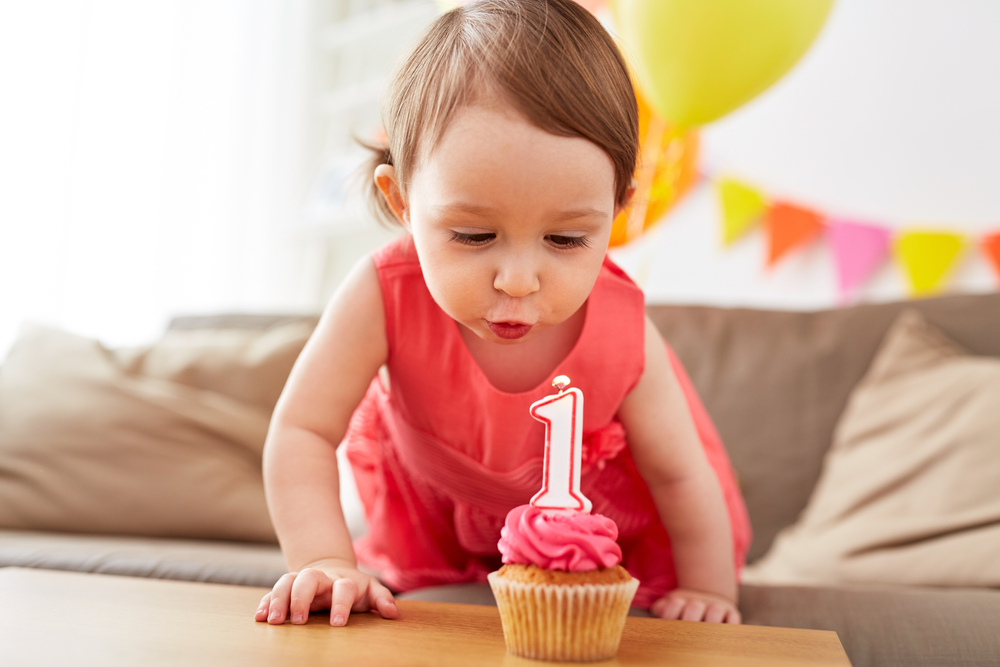 Een fotoshoot 1 jaar met een schattig meisje die haar eerste kaarsje uitblaast op een cupcake.