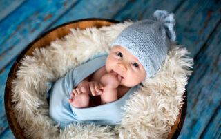 Een pasgeboren baby, gehuld in blauw, liggend in een mandje versierd met paasdecoraties. Deze foto is een creatieve combinatie van newborn fotografie en seizoensgebonden thema's, waarbij de baby wordt gepresenteerd in een paasmandje. Het kleurenschema en de decoratieve elementen voegen een speels tintje toe aan de compositie, terwijl de baby het centrale focuspunt blijft, waardoor de tederheid van de pasgeborene wordt benadrukt.